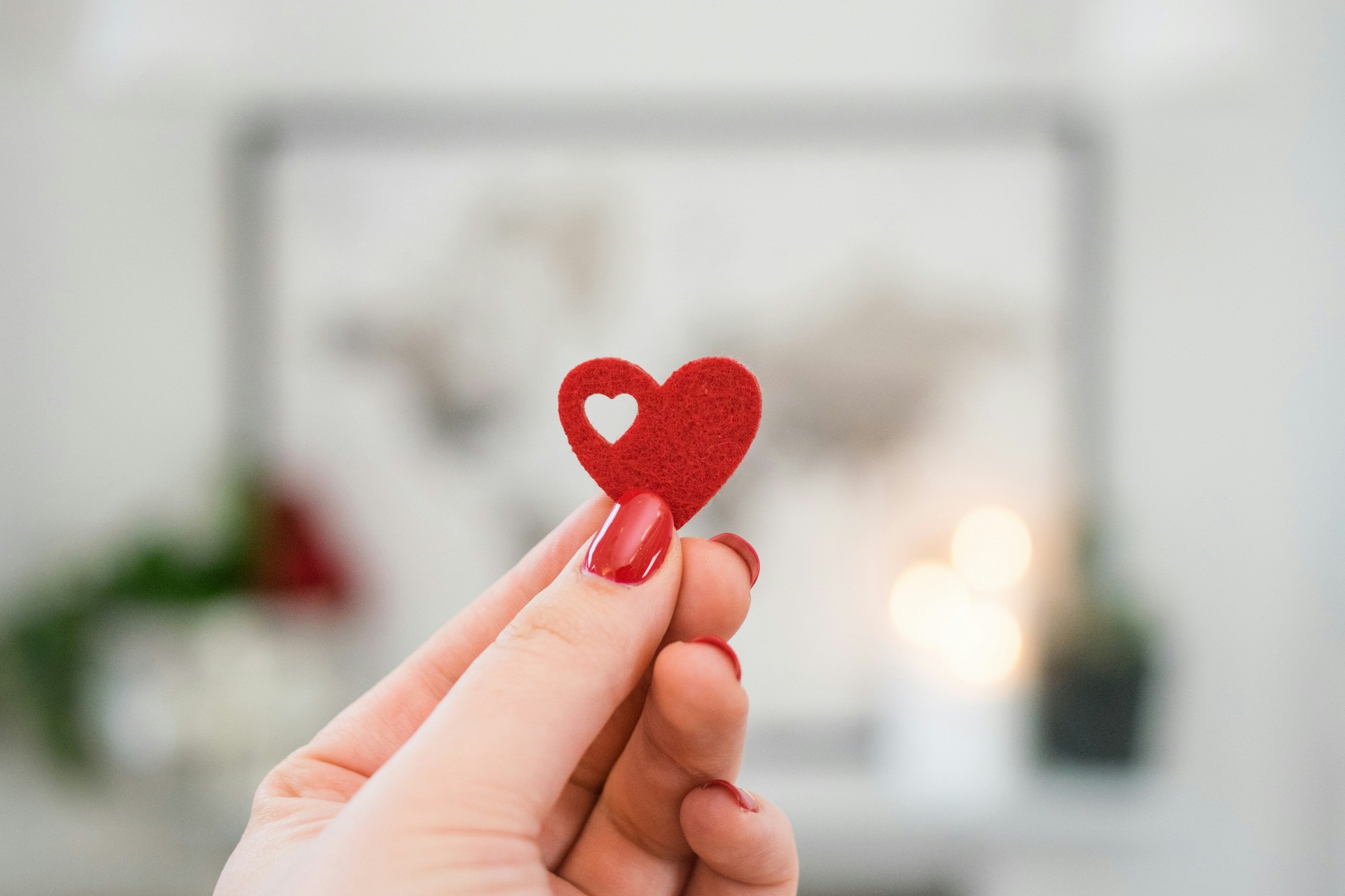 Hand hält kleines rotes Herz zwischen den Fingern